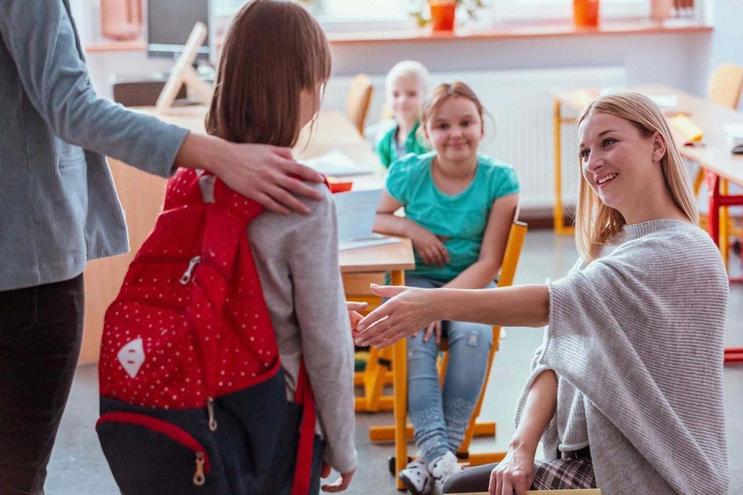 Teacher warmly greeting a young student in a small UAE classroom while classmates look on