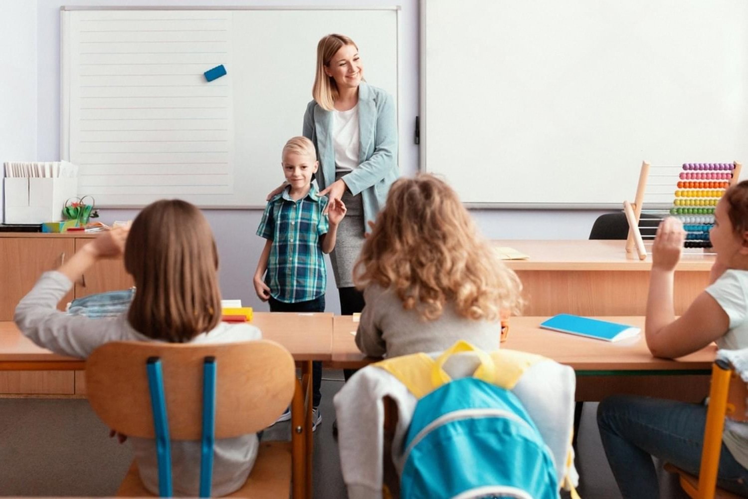 Children raising their hands in a small class as a boy answers the teacher at the whiteboard