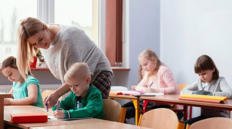Teacher leaning over to help a young boy with his writing in a small classroom