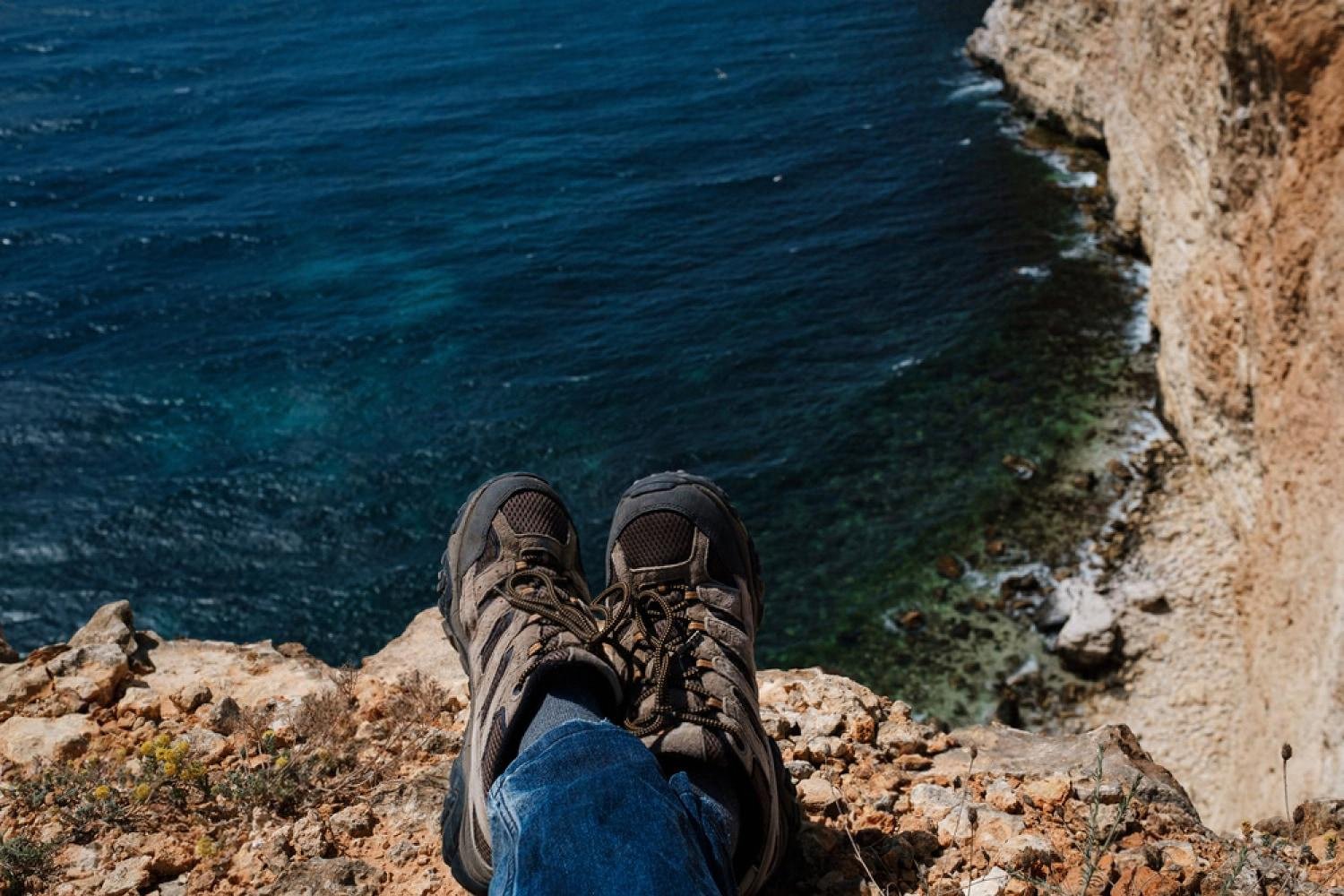 Traveller in hiking shoes sitting on a cliff edge above the sea, illustrating adventure travel insurance